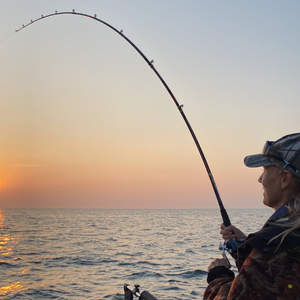 A woman casts her fishing line into a lake at sunset.