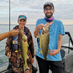 Two people stand on a small fishing boat on Lake Erie. They hold up the walleye fish they have caught for the camera. They look proud.